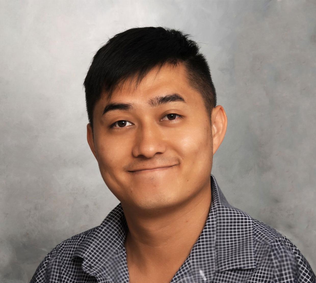 Stanley Yu smiling in front of a gray background