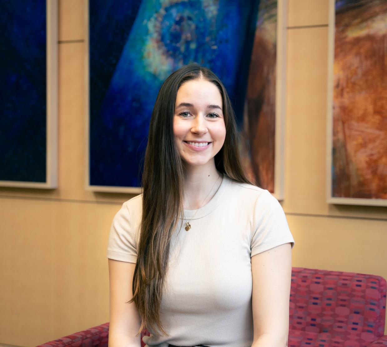 Kennedy Duff smiles for the camera in front of three colorful portraits.