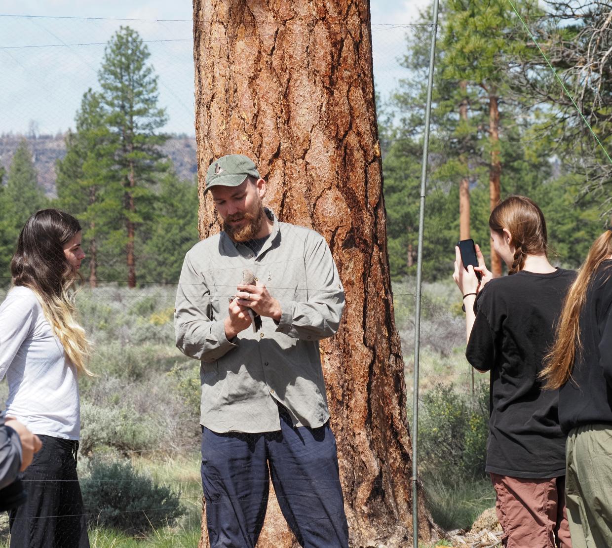 A man holds a bird and shows student. Background is trees and grass.