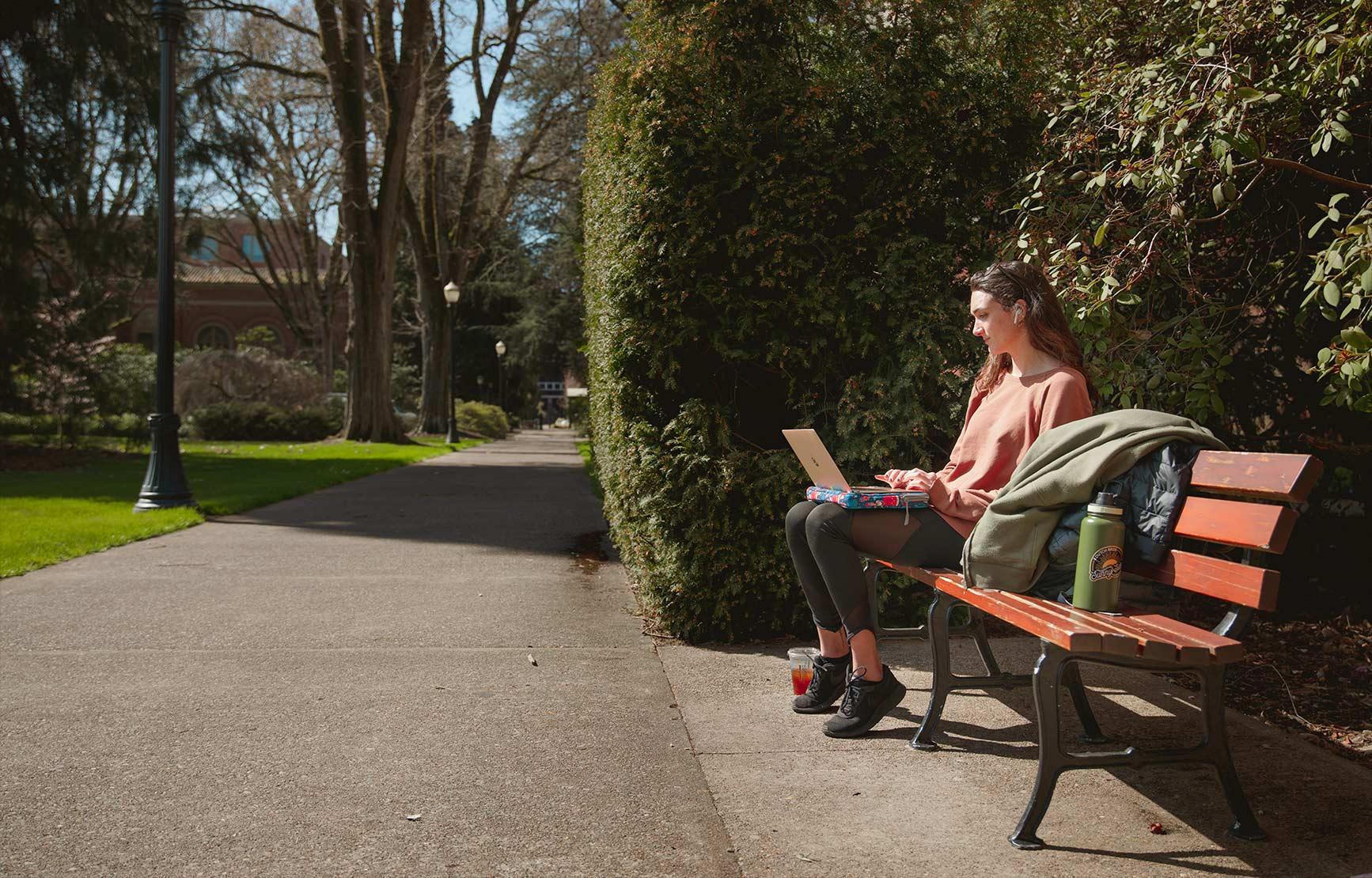 Student sitting on bench outside of the Memorial Union Quad while studying on their laptop.
