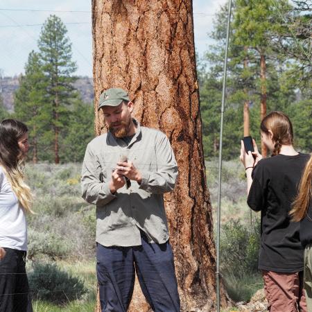 A man holds a bird and shows student. Background is trees and grass.