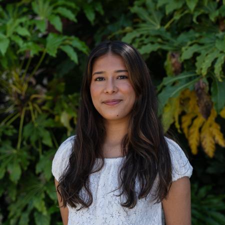 Maria Ruiz Cortes smiles for the camera in front of a green bush.