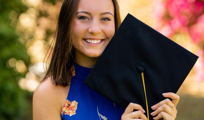 Jade Sentker holding graduation cap in front of shrubbery