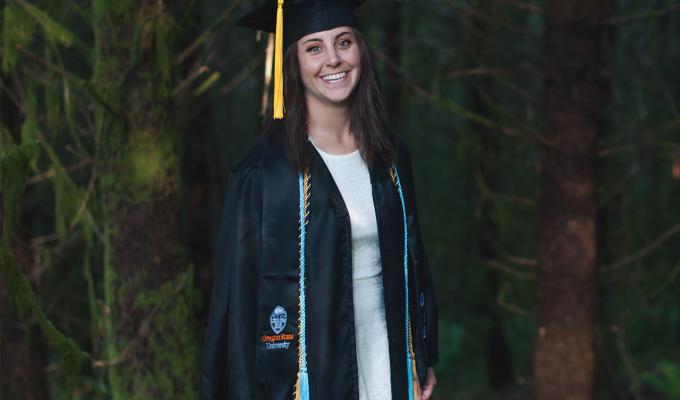 Taylor Robinson in graduation gown, standing in forest