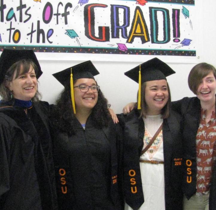 A group of graduates and Lori Kayes standing in front of a sign reading "Hats off to the Grad!"