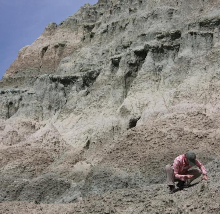 Student kneeling at the foot of the John Day Fossil Beds