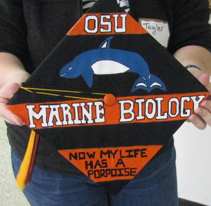 Close up of a graduation cap with a porpoise and the pun "Now my life has a porpoise"