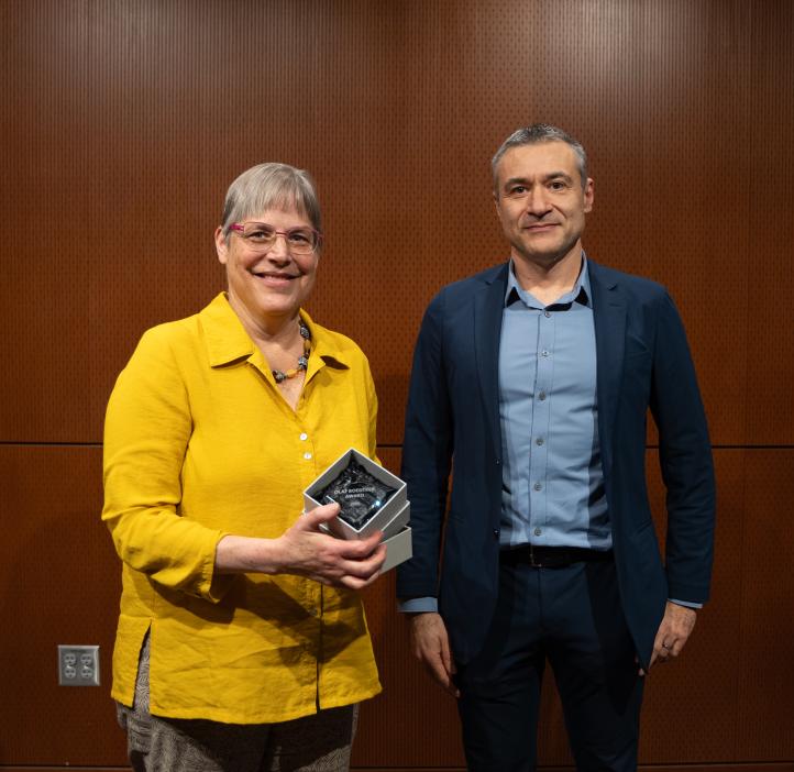 A woman in a yellow shirt holds a glass award standing next to a man in a blue suit.